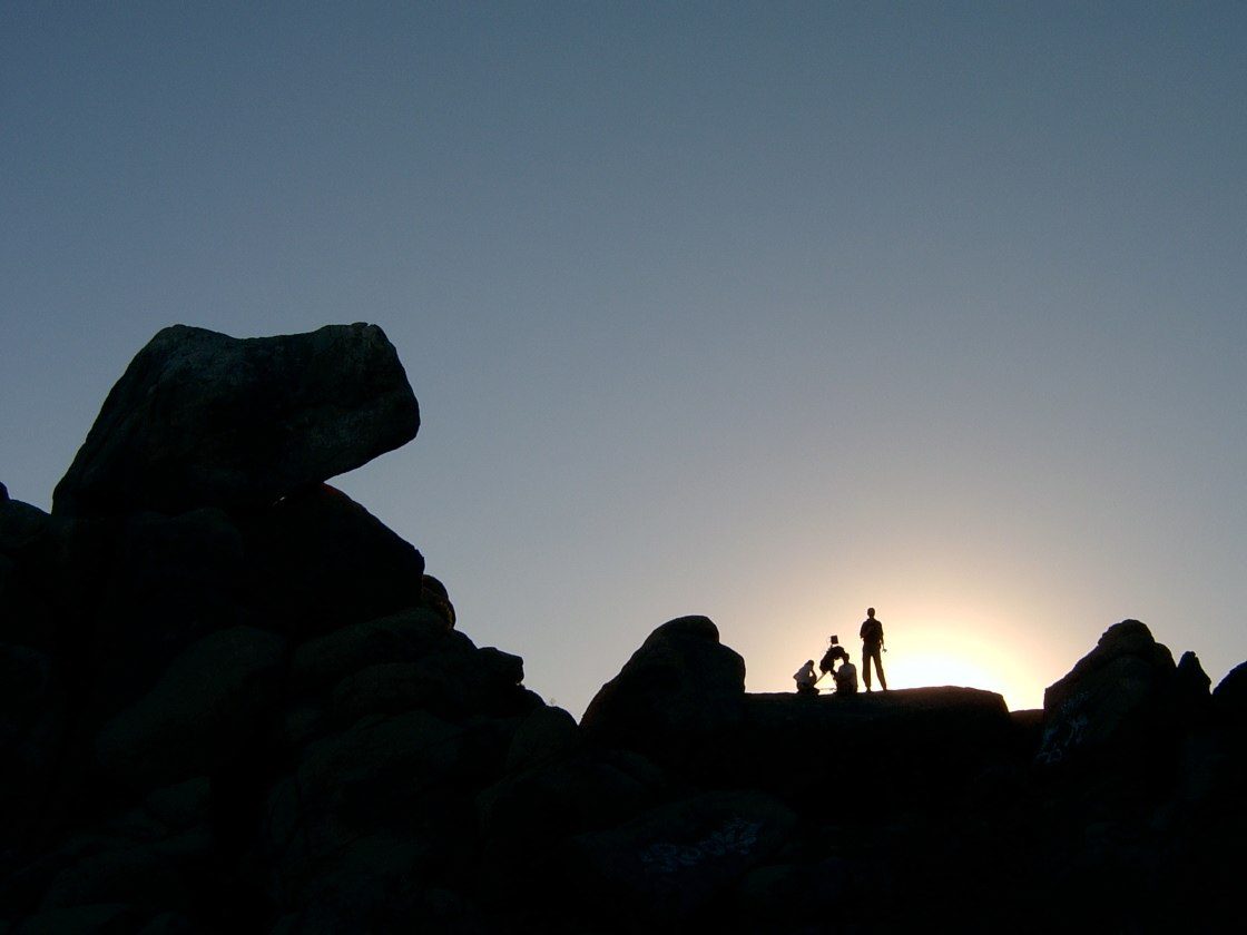Men on rock watching sunset.